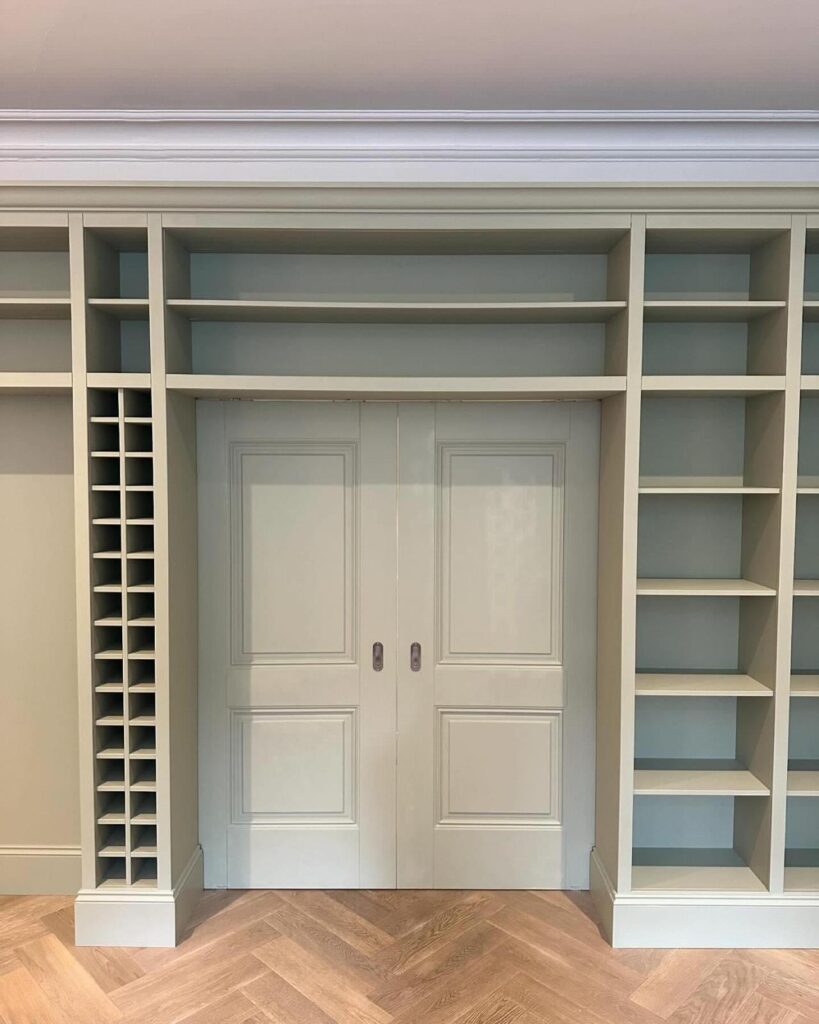 Sage green fitted bookcase and wine rack built around painted double doors, with herringbone oak floor, by R3 Carpentry
