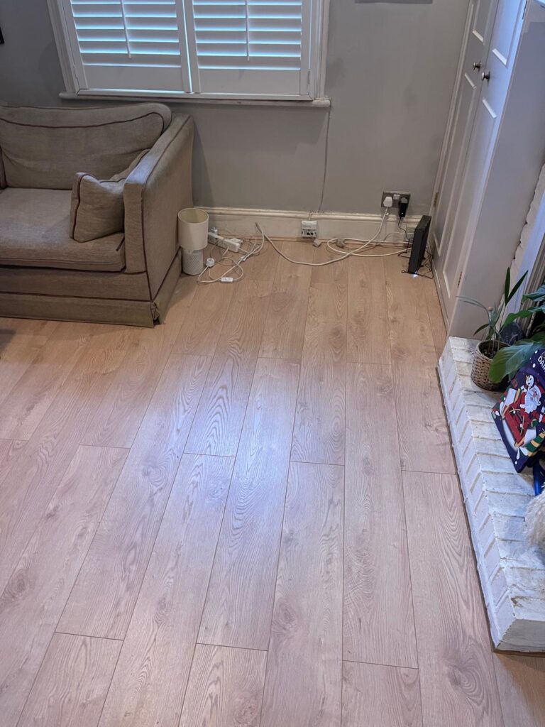 Light oak flooring fitted in a living room with shutters and exposed brick hearth