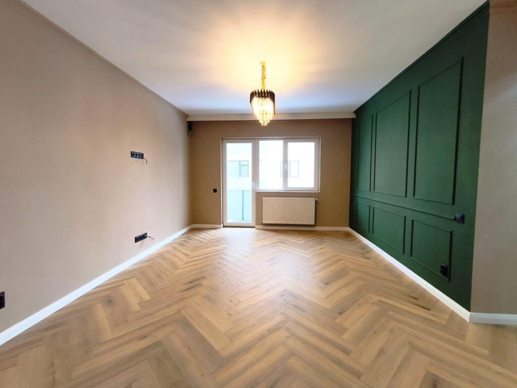 Herringbone wood flooring in a finished living room with green panelled wall