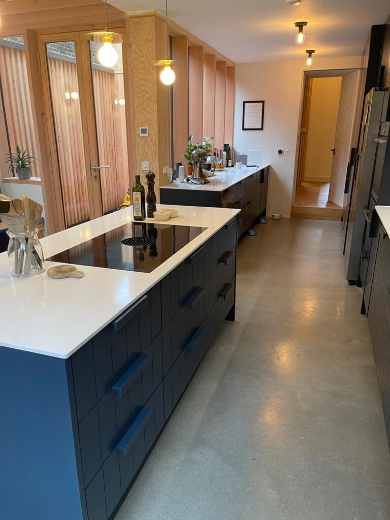 Navy blue kitchen island with white quartz worktop, induction hob and polished concrete floor, fitted by R3 Carpentry