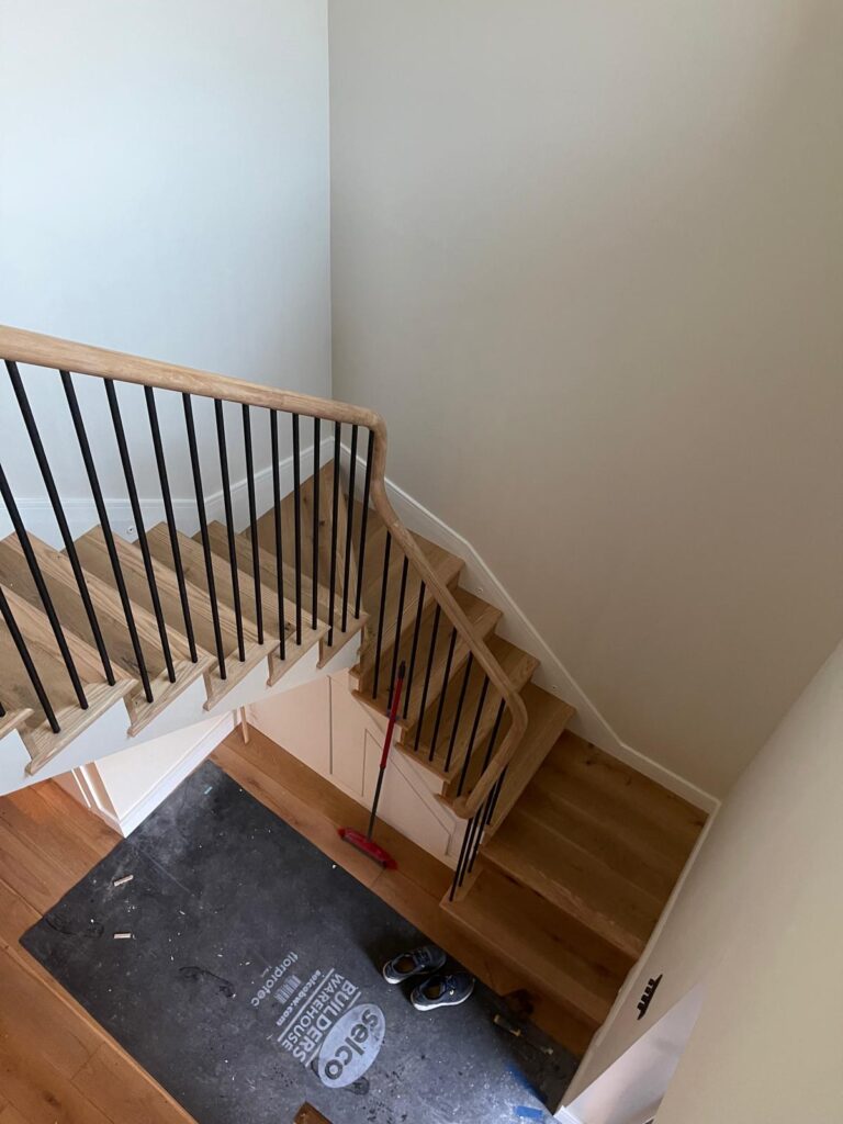Oak staircase with oak handrail, black metal spindles and a half-turn winder, fitted by R3 Carpentry